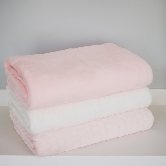 Tres frazadas polar apiladas en tonos rosa y blanco suave-rosa