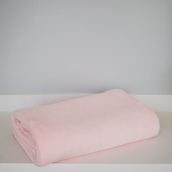 Frazada polar rosa lisa enrollada sobre superficie blanca-rosa