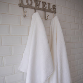 Dos toallas blancas colgadas en ganchos bajo letrero "TOWELS-blanco