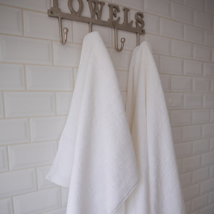 Dos toallas blancas colgadas en ganchos bajo letrero "TOWELS-blanco
