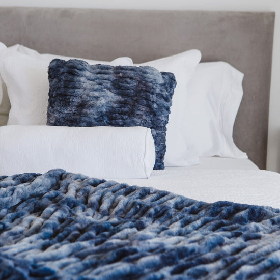 Cama con manta azul texturizada, almohadas blancas y cabecero gris-azul