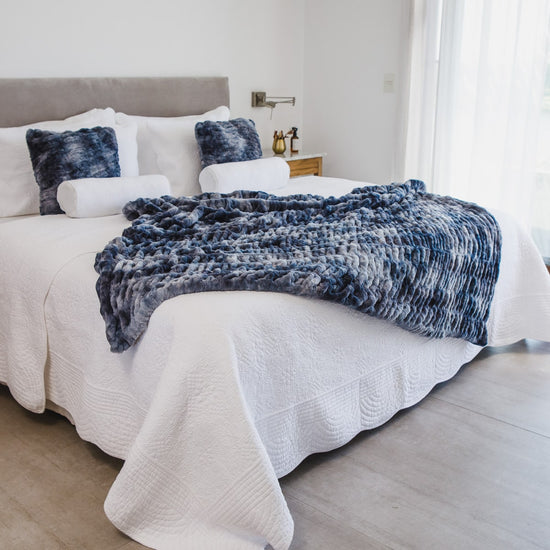 Manta azul texturizada sobre cama blanca con almohadas decorativas-azul