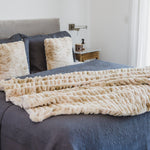 
                    
                      Manta beige texturizada sobre cama con almohadas y sábanas azules-beige
                    
                  