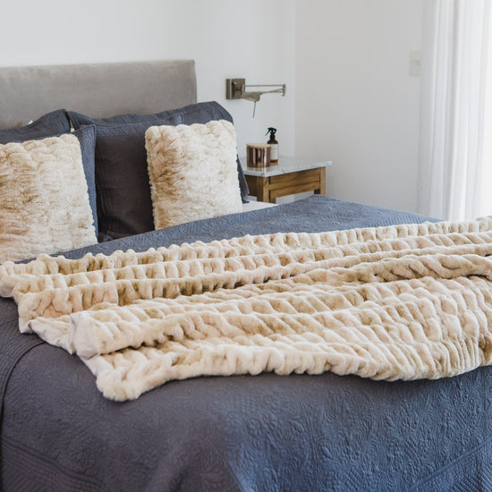 Manta beige texturizada sobre cama con almohadas y sábanas azules-beige