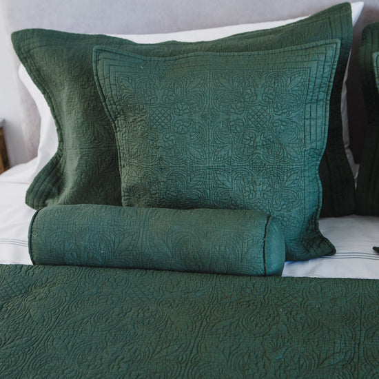 Almohadas verdes acolchadas con patrón floral sobre cama blanca-verde