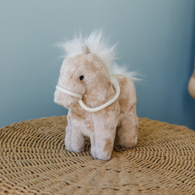 Peluche caballo beige con crin blanca y arnés sobre tapete tejido-marron