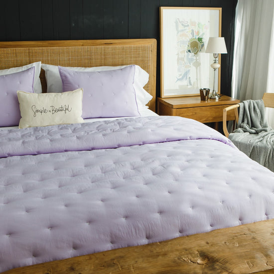 Cubrecama acolchado lila con almohadas a juego en cama de madera-lila