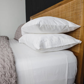 Cama con sábanas blancas plisadas y dos almohadas blancas sobre cabecero-blanco