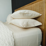 
                    
                      Cama con sábanas y almohadas beige sobre cabecero de madera y ratán-natural
                    
                  