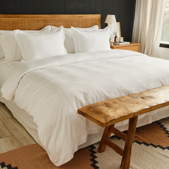 Cama moderna con funda de edredón blanca y banco de madera al pie-blanco
