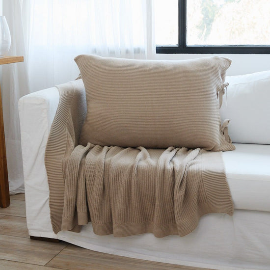 Funda de almohada Ginger 3 beige en sillón blanco junto ventana-