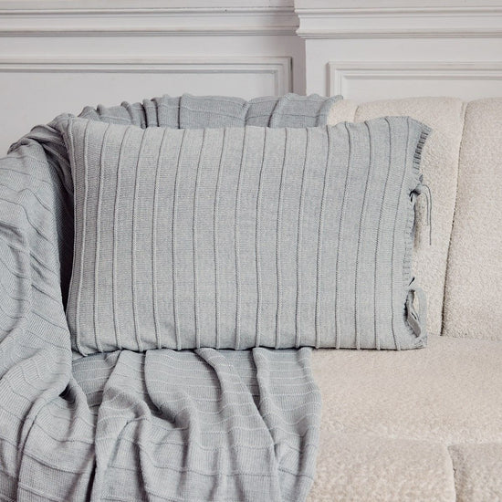 Funda de almohada gris con textura acanalada sobre sofá blanco-