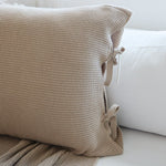 
                    
                      Funda de almohada beige con textura tejida y detalles de lazos decorativos-
                    
                  