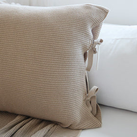 Funda de almohada beige con textura tejida y detalles de lazos decorativos-