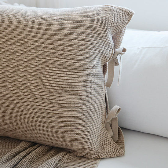 Funda de almohada beige con textura tejida y detalles de lazos decorativos-