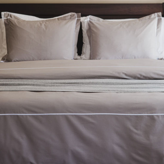 Cama con funda edredón gris claro y dos almohadas blancas decorativas-gris