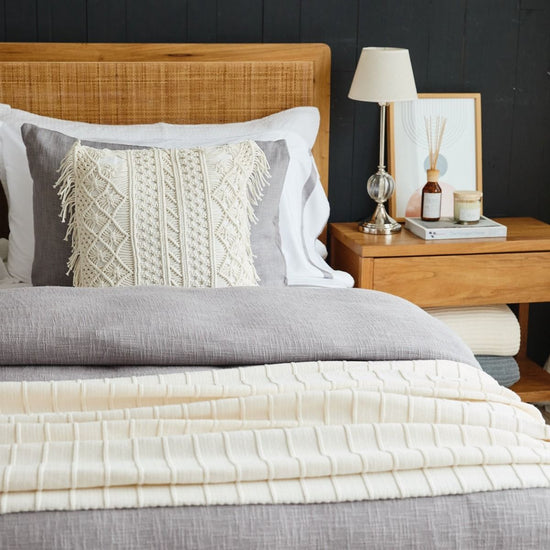 Cama con funda de edredón gris, almohadas decorativas y mesita de noche de madera-