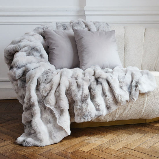 Sofá beige con almohadas y manta gris en piso de madera-