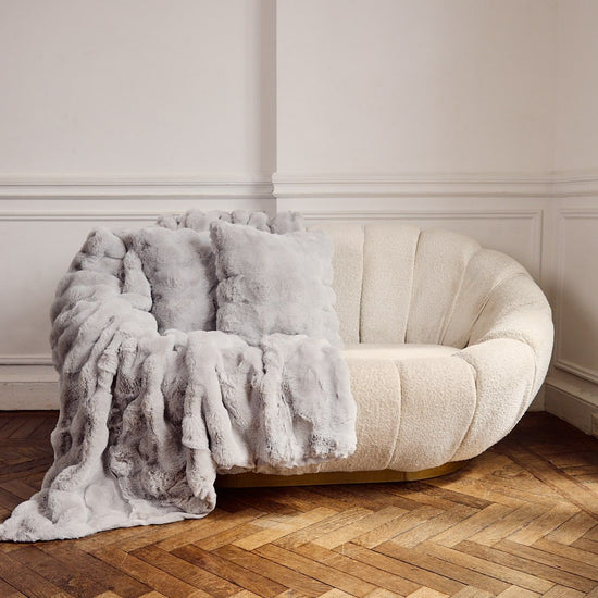Sillón redondo beige con manta gris en piso de madera-gris