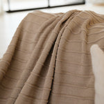 
                    
                      Manta tejida beige con patrón geométrico doblada sobre sofá-beige
                    
                  