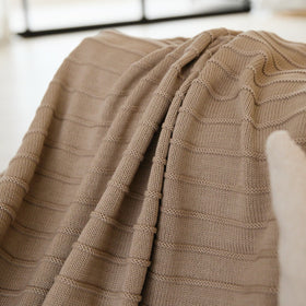 Manta tejida beige con patrón geométrico doblada sobre sofá-beige