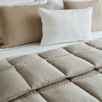 
                    
                      Edredón beige acolchado con almohadas decorativas en cama blanca-beige
                    
                  