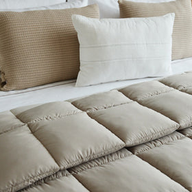 Edredón beige acolchado con almohadas decorativas en cama blanca-beige
