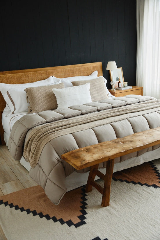 Cama con edredón beige, almohadas y banco de madera al pie-beige