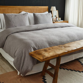 Funda de edredón gris en cama con cabecero de ratán y banco de madera-gris