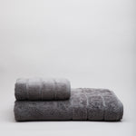 
                    
                      Set de toallas grises oscuras apiladas sobre fondo blanco-gris oscuro
                    
                  