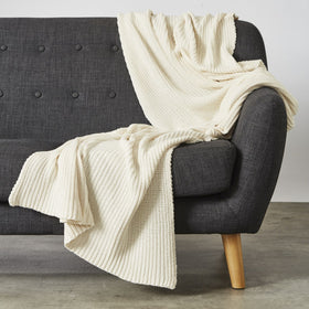 Manta de lana crema acanalada sobre sillón gris oscuro con patas de madera-natural