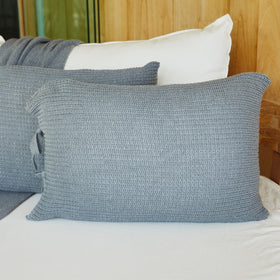 Funda de almohada gris texturizada sobre cama con almohadas blancas-gris