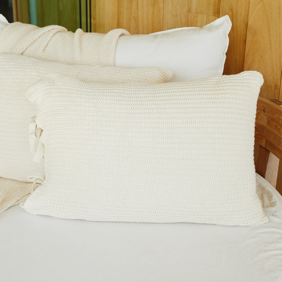 Funda de almohada tejida color natural sobre cama de madera-natural