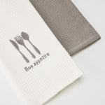 
                    
                      Dos repasadores, uno blanco con cubiertos y texto Bon appetit, otro gris-gris
                    
                  