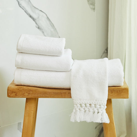 Toallas blancas apiladas en banco de madera en baño-blanco