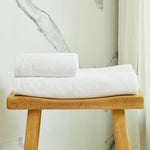 
                    
                      Toallas blancas premium apiladas sobre banco de madera natural-blanco
                    
                  