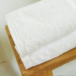 
                    
                      Toalla blanca premium doblada sobre superficie de madera-blanco
                    
                  