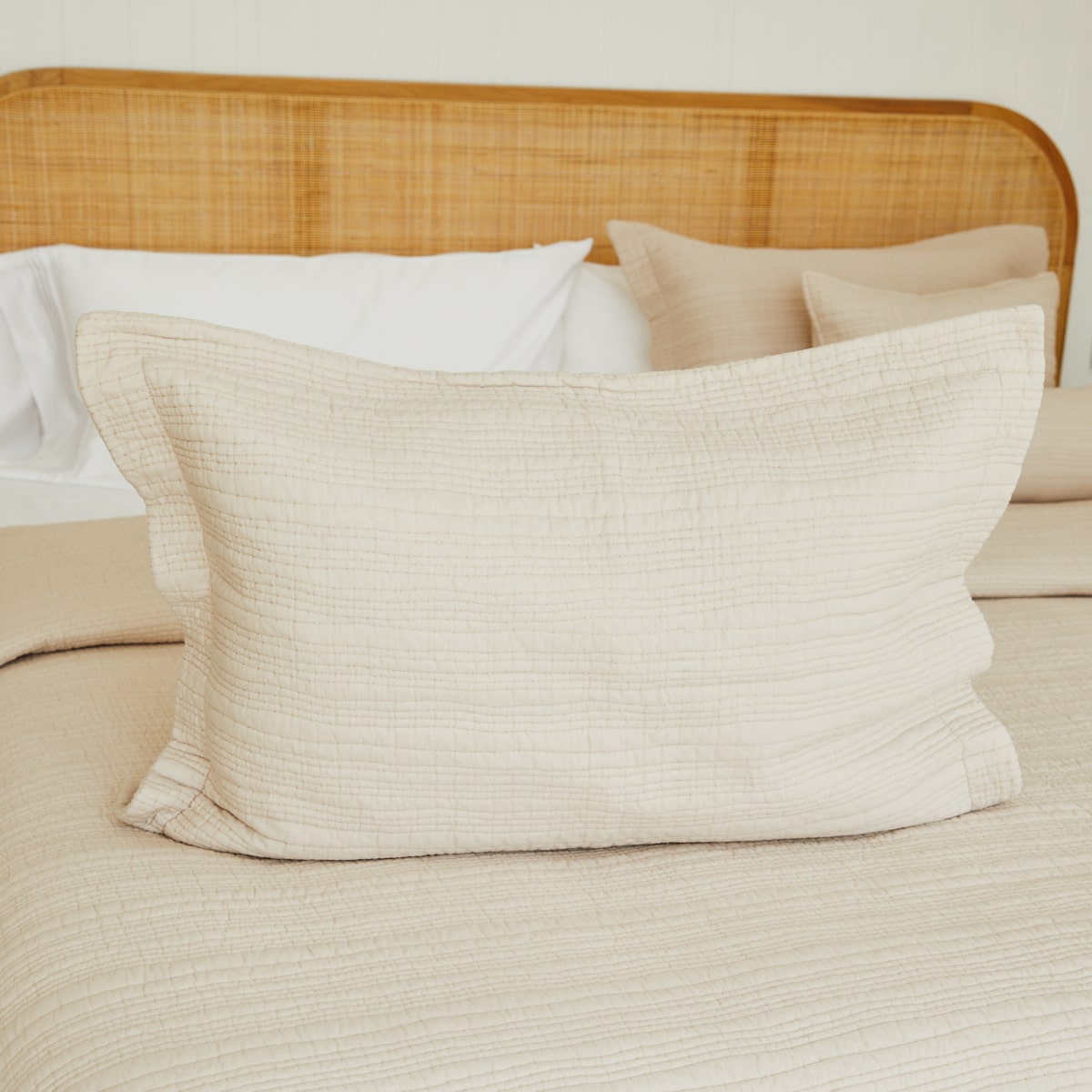 Funda de almohada beige texturizada sobre cama con cabecero de ratán-beige