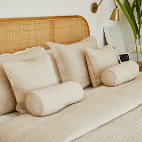 Cubrecama beige con almohadas decorativas y cojines cilíndricos en cama-beige