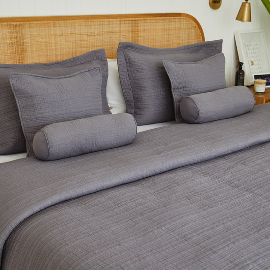 Cama con juego de sábanas gris y almohadas decorativas cilíndricas-gris