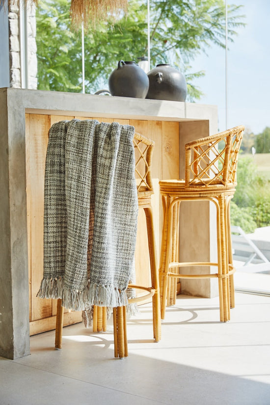 Manta Santorini gris colgada en mostrador de madera con sillas de ratán-gris