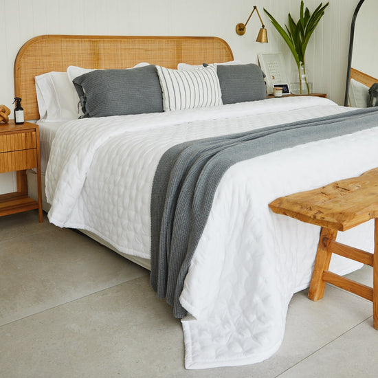 Cubrecama blanco sobre cama con almohadas grises y madera natural-blanco