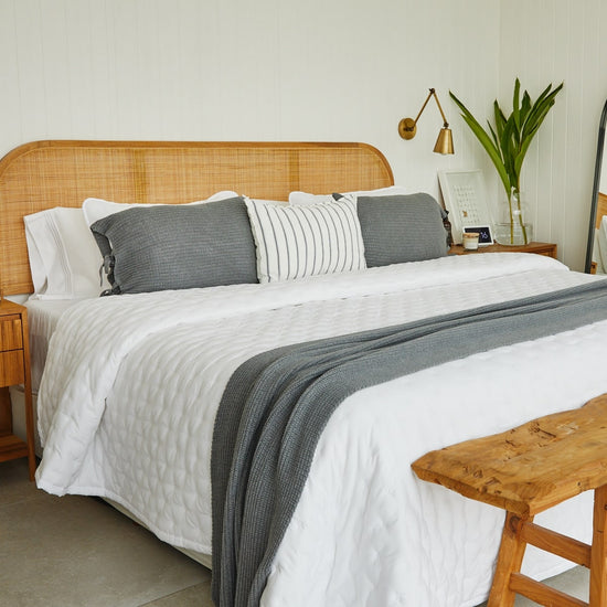 Cama con almohadas grises y blancas en cabecera de ratán natural-gris