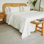 
                    
                      Manta de algodón beige sobre cama con cabecero de ratán y almohadas blancas-beige
                    
                  