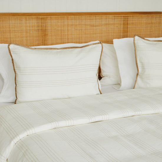 Cama con manta beige y almohadas blancas con ribete marrón-beige