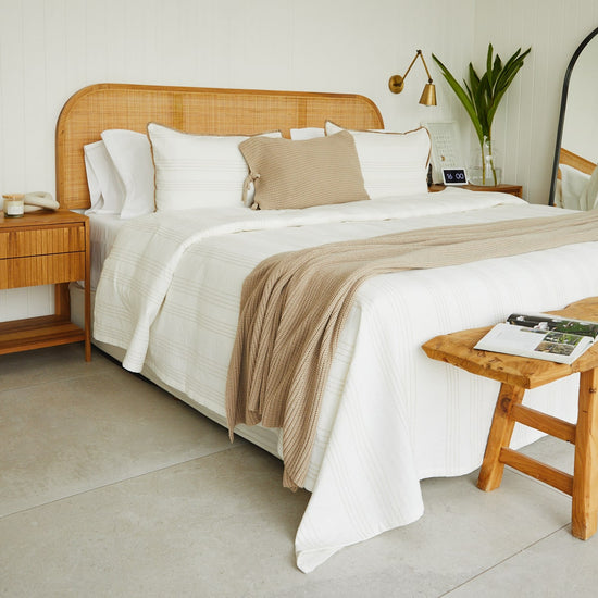 Cama de madera con manta beige de algodón sobre sábanas blancas-beige