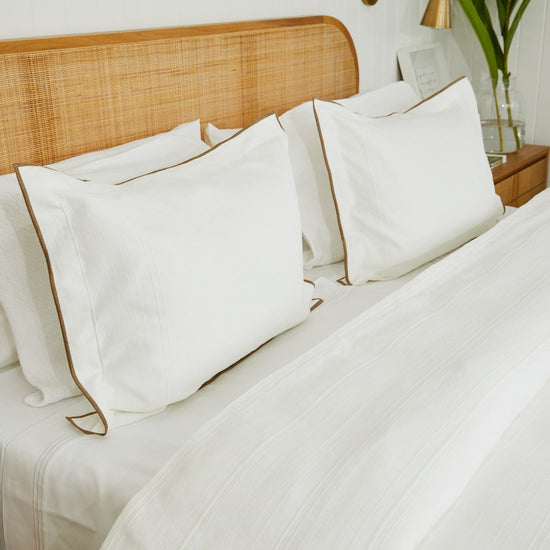 Cama con funda de edredón blanco, almohadas y cabecero de ratán-blanco