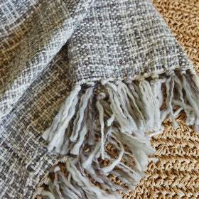Manta gris Santorini con flecos blancos sobre superficie tejida-gris