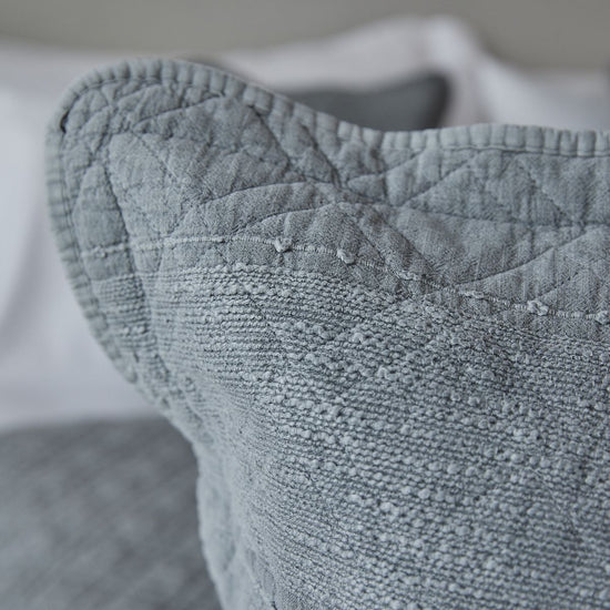 Detalle texturizado de funda almohada gris con costuras y tejido acolchado-