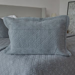
                    
                      Funda de almohada gris con patrón acolchado diamante sobre cama-
                    
                  